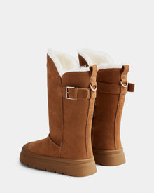 The Rudsak KLAIR - L225027 Tan features tall brown suede winter boots with white wool lining, side buckle detail, and flat rubber soles, shown from the back at an angle on a plain light background.