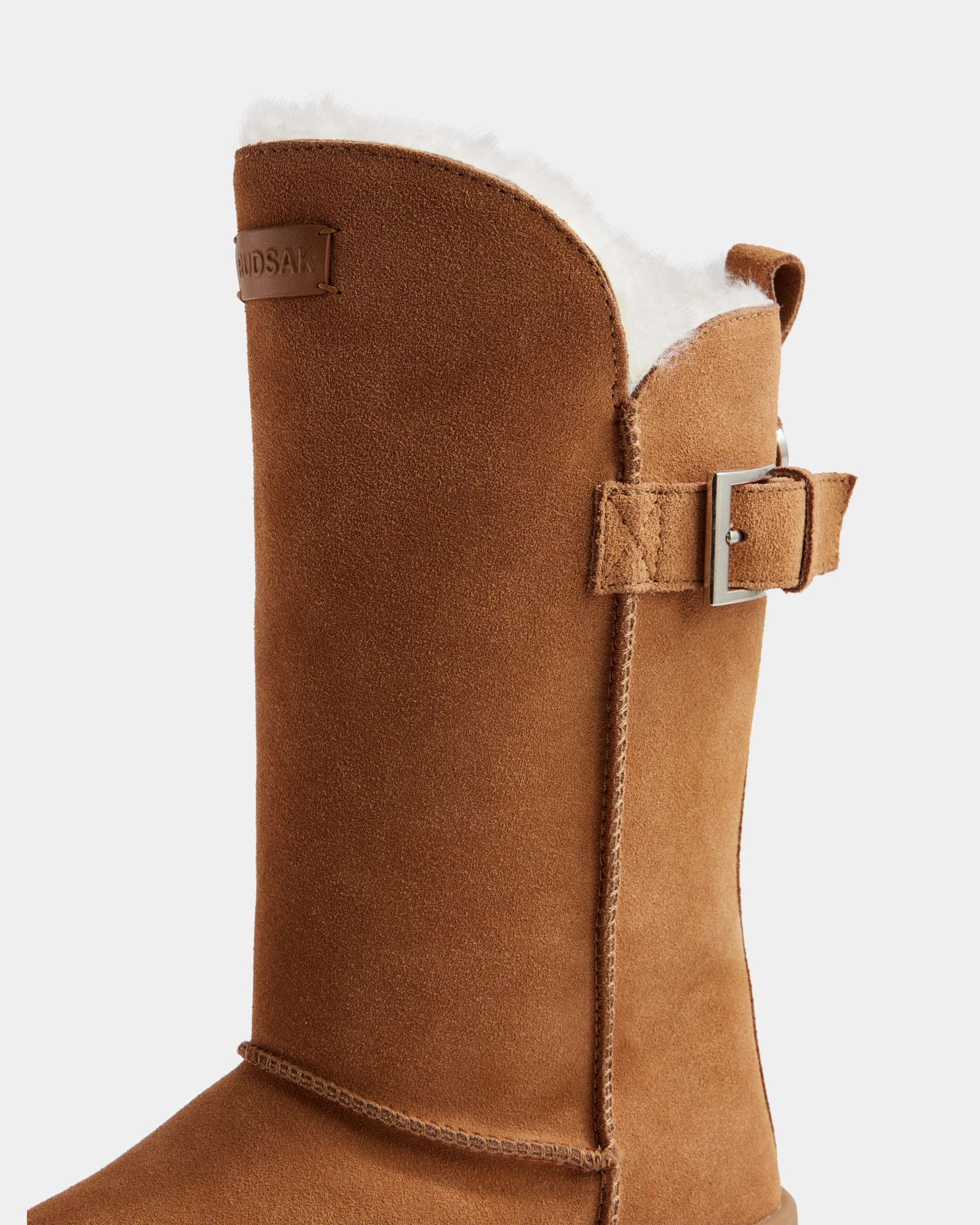 A close-up of Rudsak KLAIR - L225027 Tan women’s mid boots in tan suede with white wool lining, side buckle strap, and visible stitching, set against a plain light background.