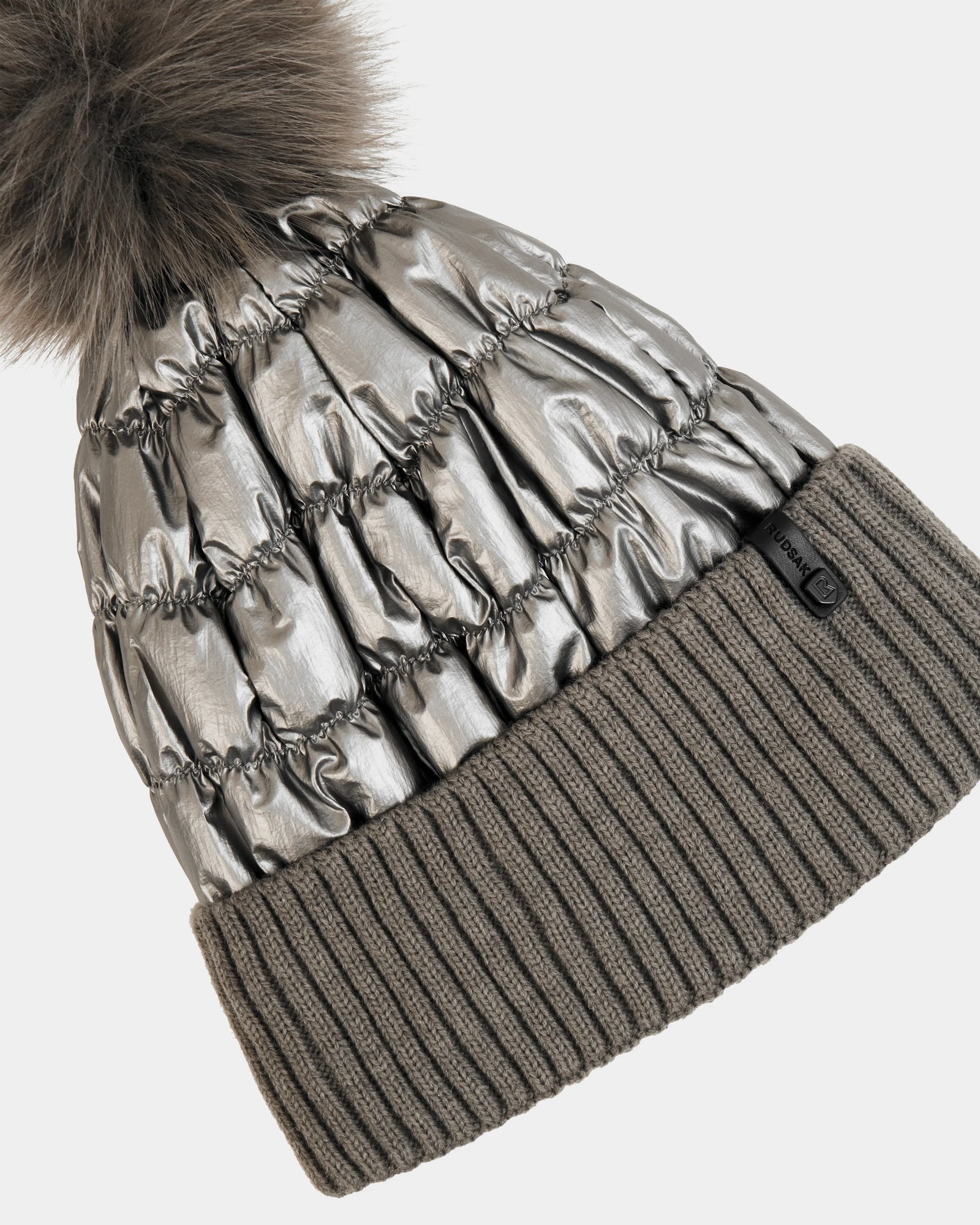 The Rudsak LANYA - L423514 Pewter is a metallic silver quilted women’s pom pom hat with a large faux fur top and wide ribbed gray knit cuff—perfect for standout winter style and cozy warmth.