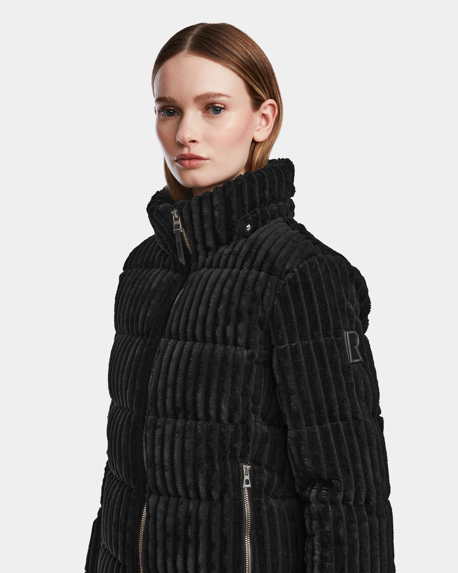 A woman with straight, shoulder-length hair wears the MIRRY FF - L124507 Black RDS-certified down short puffer jacket with a ribbed quilted design, high collar, and visible zippers, standing against a plain white background.