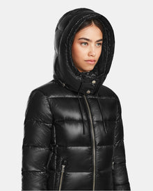 A woman in a shiny black Rudsak MIRRY S - L123545 quilted down coat with the hood up, glances to the side against a plain light background.