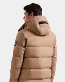 A man is seen from the back and side wearing the Rudsak RICKY - M123502 Sand men's quilted down parka, featuring a hood, black upper arm patch, and black label on the hood. Set against a white background—ideal for winter style.