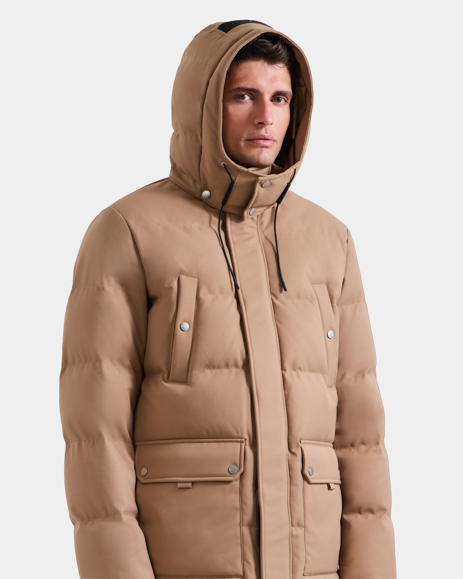 A man models the Rudsak RICKY - M123502 Sand parka with a hood, front pockets, and button details against a plain white background, highlighting classic winter style.