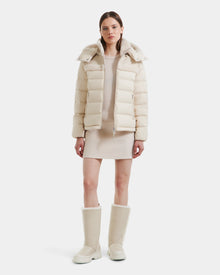 A woman faces forward in a modern look, wearing the Rudsak SANDRA - 8125612 Vanilla women’s shearling puffer jacket with a matching short dress and knee-high boots. She has straight brown hair and a neutral expression against a white background.