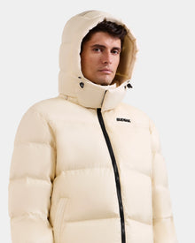 A man wears the STEFANO - 6125574 Vanilla men’s down puffer by Rudsak, featuring a hood and black zipper, with 