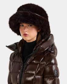 A woman models the Rudsak YURI - L425538 Espresso puffer jacket with vegan-leather trim and a matching faux-fur bucket hat, looking at the camera against a plain light background—a chic winter accessory ensemble.