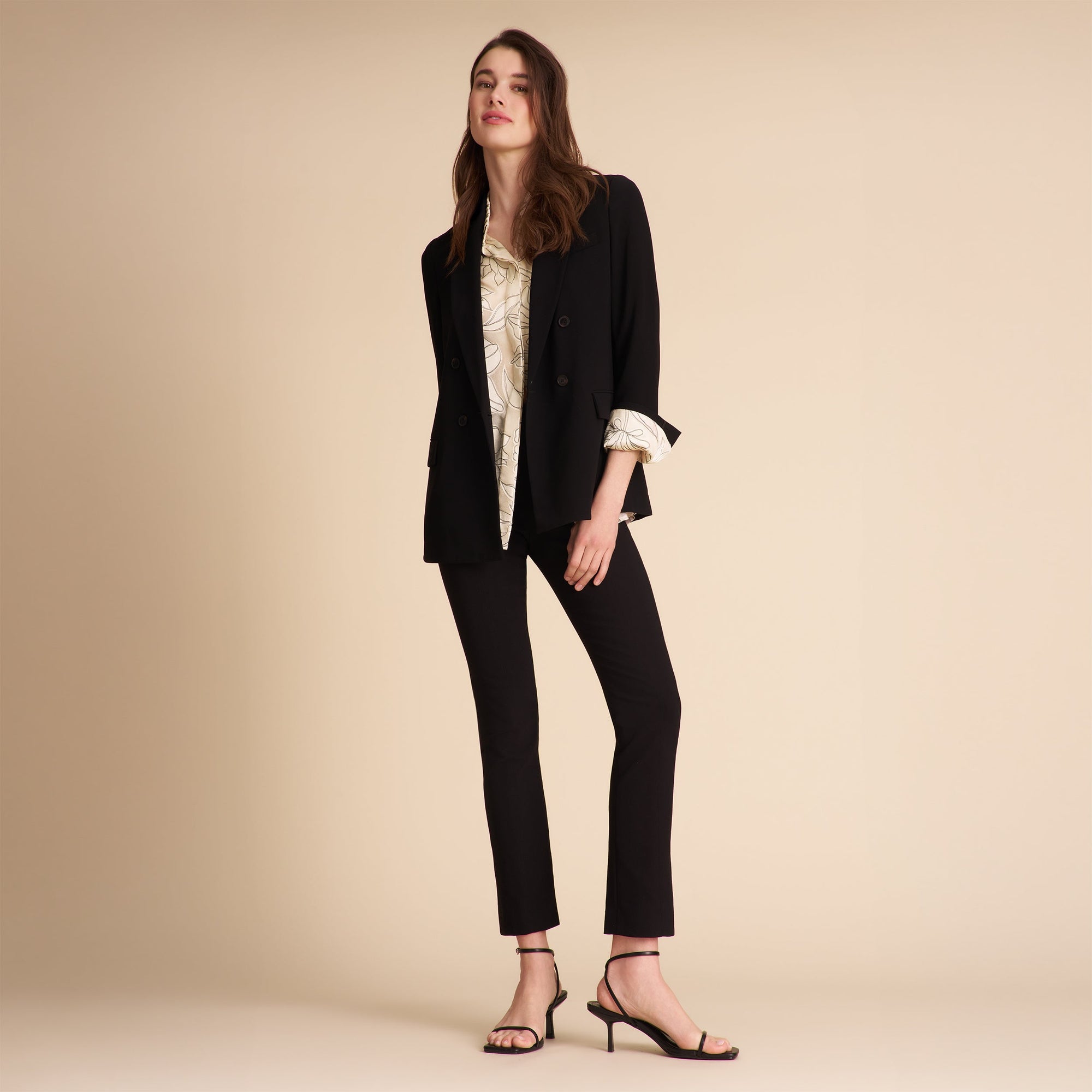 Person wearing black pants and a patterned top on a beige background | Exclude