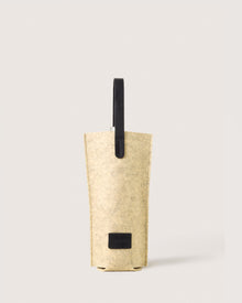 The graf lantz Hana Bottle Bags collection includes a minimalist beige felt wine tote made from Merino wool, featuring leather handles and a small black label near the base, all set against a plain background.