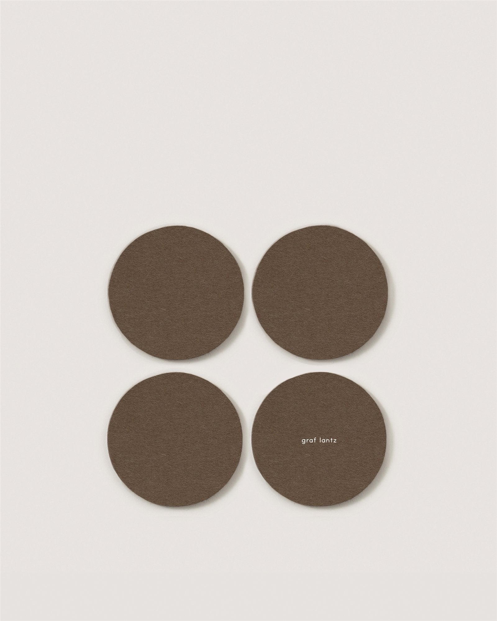 Four round, brown Merino wool coasters by Graf Lantz are arranged in a square on a white background. One features "graf lantz" in small white text near the edge—a refined detail for eco-friendly home decor.