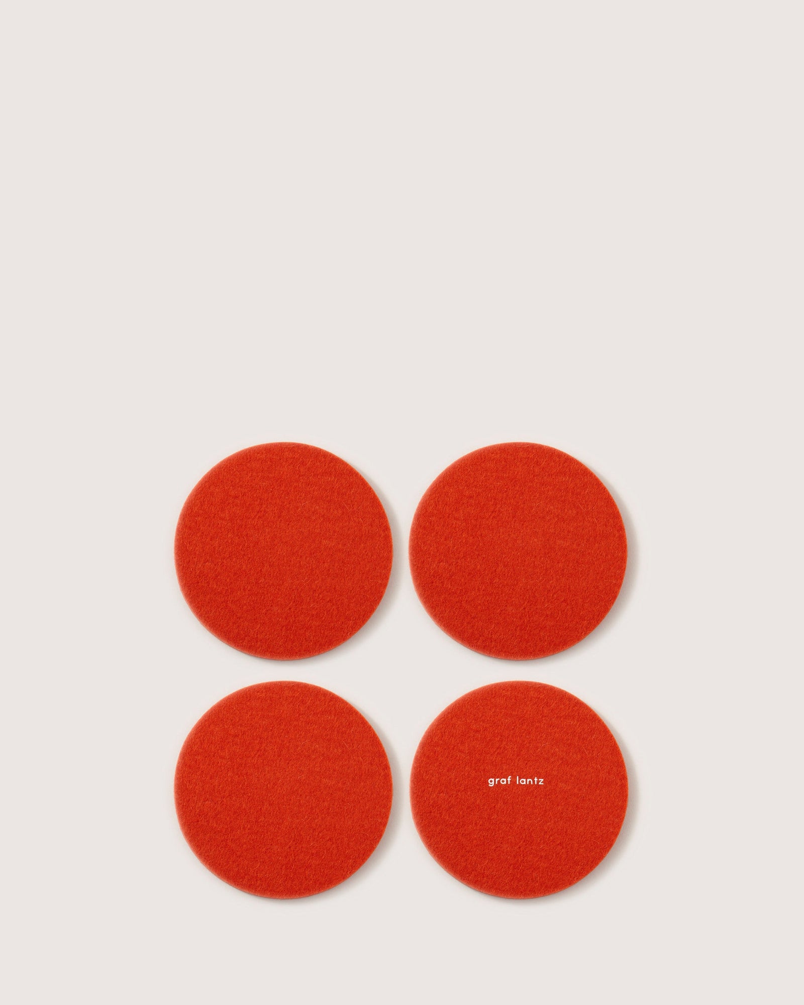 Four red circular felt coasters, crafted from luxurious German Merino wool by graf lantz, are set in a square on a white background. One coaster is elegantly printed with graf lantz in small white letters.
