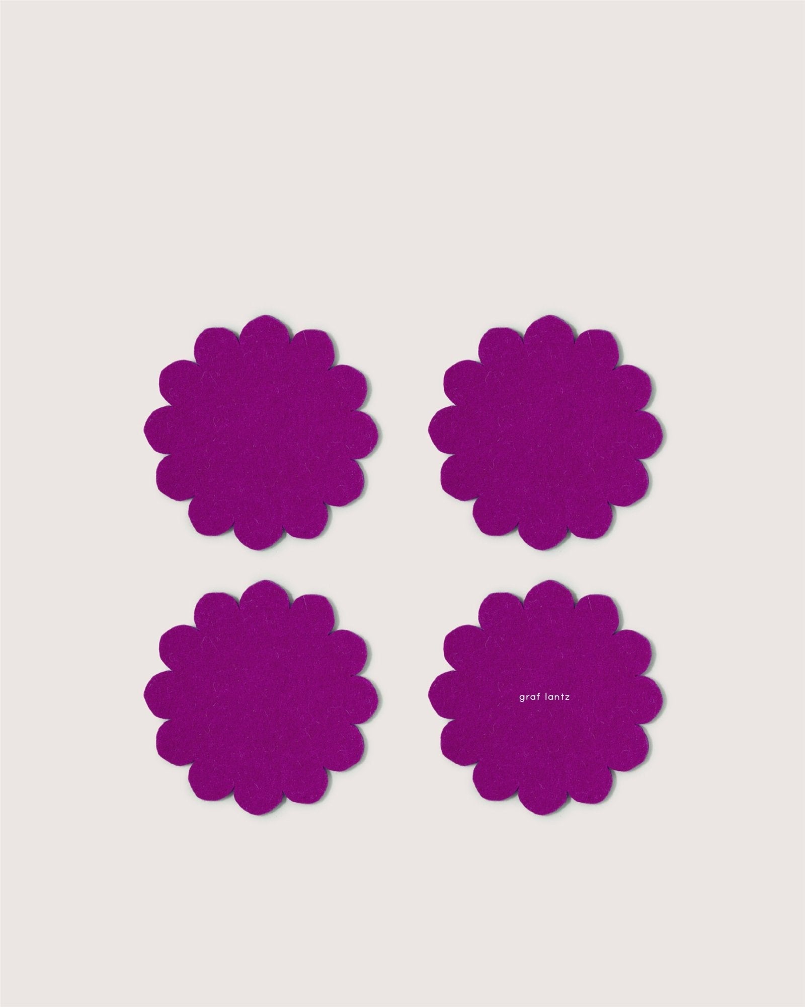 Four purple floral coasters by Graf Lantz, crafted from Merino wool, are arranged in a square on a light background. One displays the Graf Lantz brand in small white letters, offering stylish protection for your table.