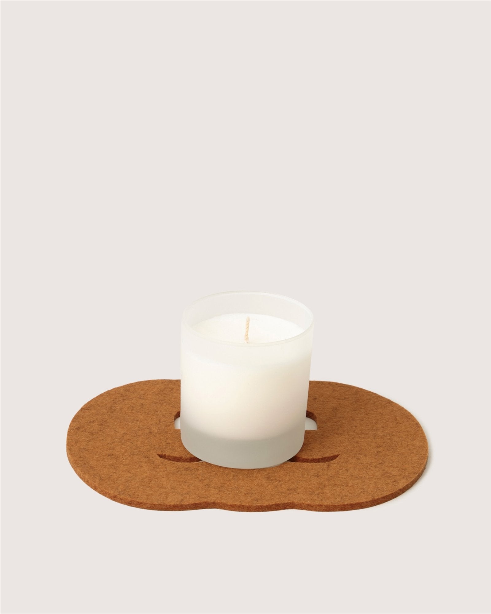 A white Graf Lantz candle in a frosted glass holder rests on a brown, irregular cork mat against a simple light background.
