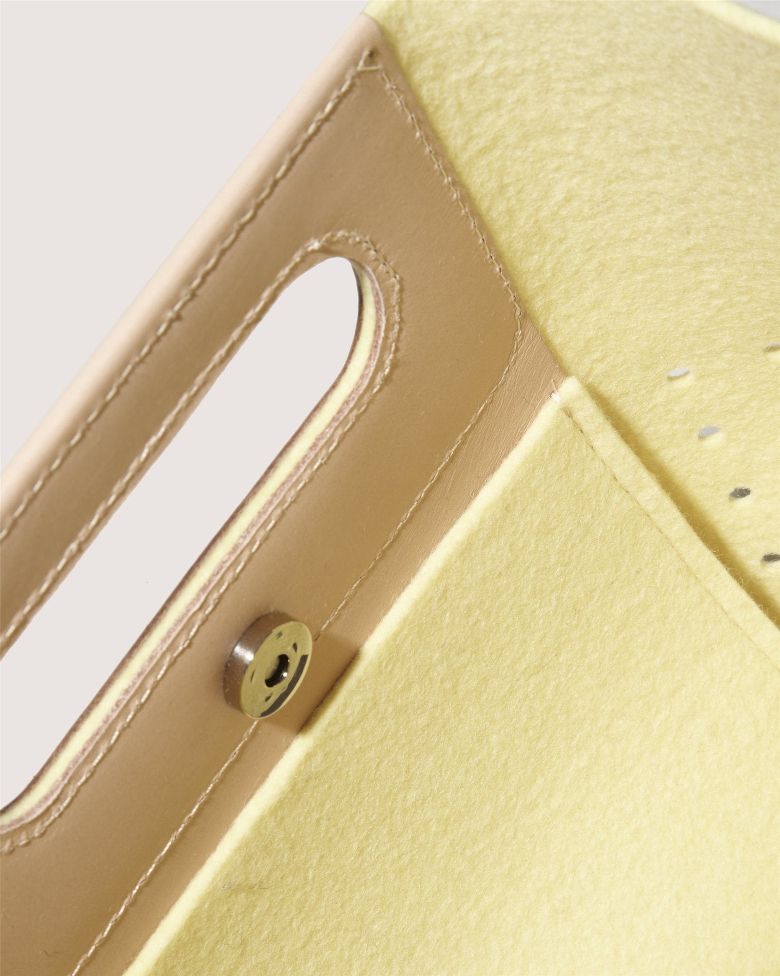 Close-up of a minimalist yellow Asobi Bag by Graf Lantz, crafted from Merino wool. It features a rectangular cutout handle, metal snap button closure, and leather trim along the edge.
