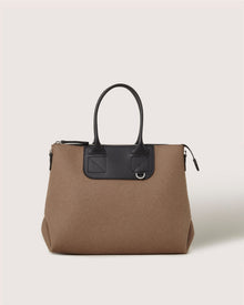 A brown Graf Lantz handbag with black leather handles and trim, featuring a rectangular zippered top, a subtle metal ring on the front, set against a light beige background.