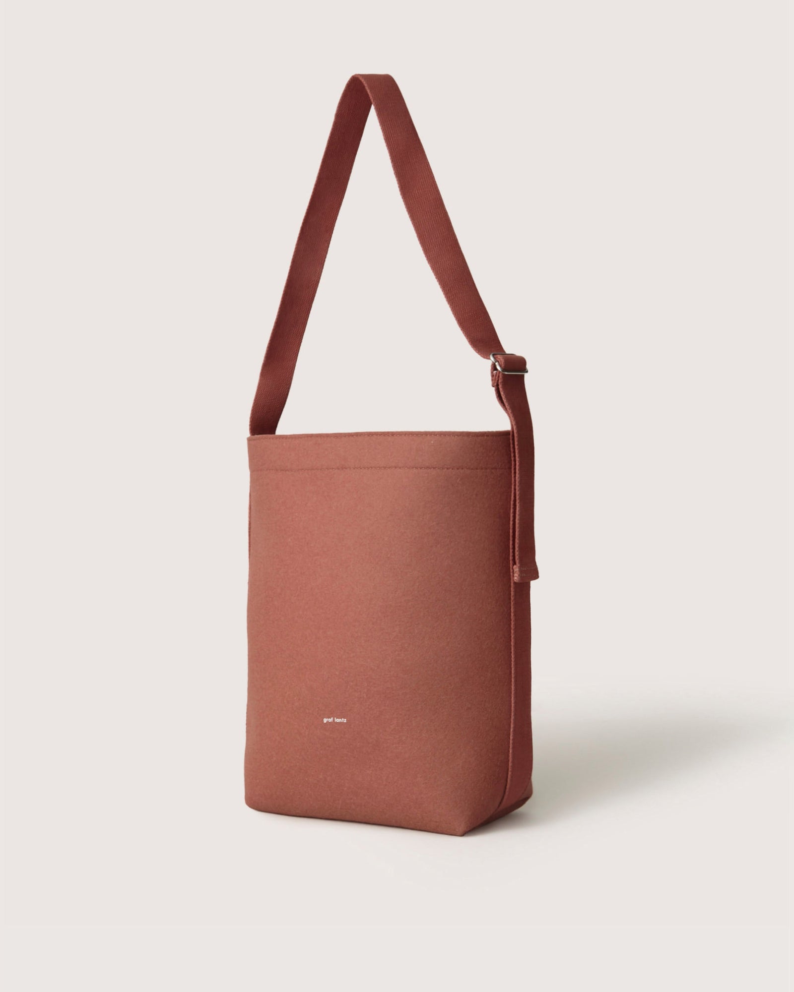 The Graf Lantz brown fabric shoulder bag, designed for everyday functionality, features a single adjustable strap and minimalist design. Showcased against a plain white background, this sustainable accessory with a subtle logo adds effortless elegance to any outfit.