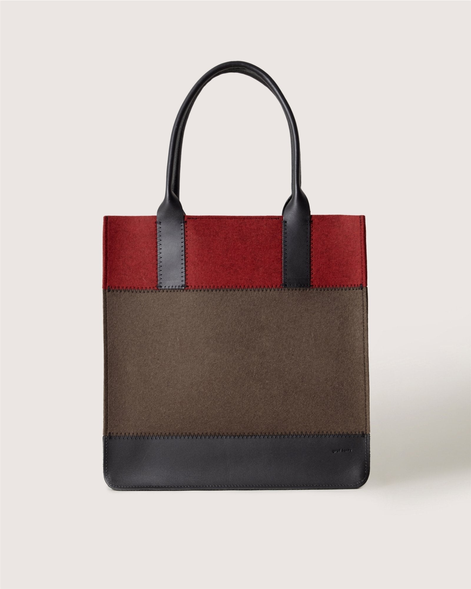 A structured Graf Lantz tote bag with black handles, a dark red top, brown middle section, and black bottom trim is displayed against a plain light background.