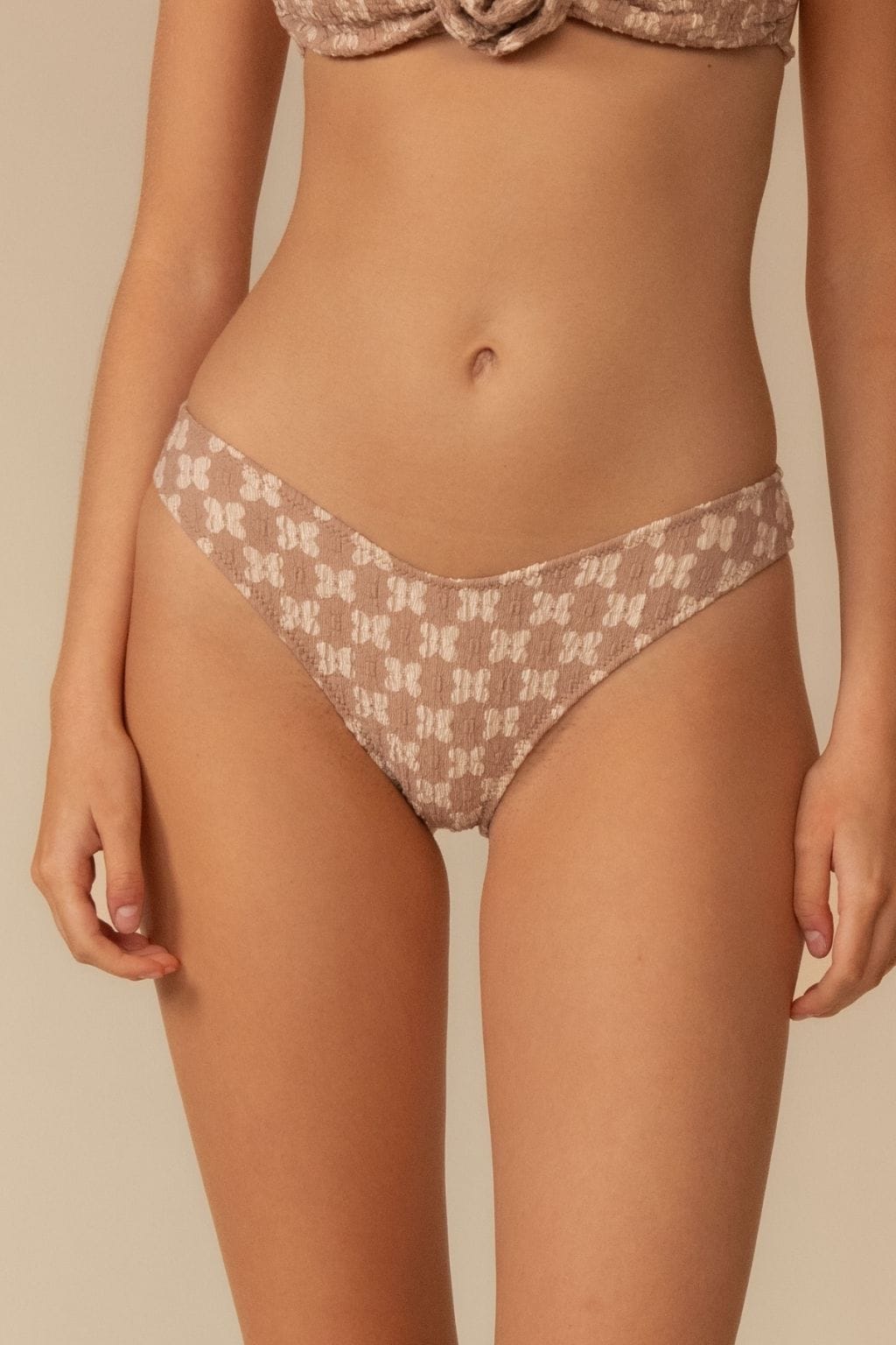 Beige lace bikini bottom with zig-zag stitching and geometric pattern, shown on model from waist to thigh.