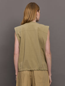 Model wears a wide shoulder, khaki zip up vest with tactical symmetrical front cargo pockets at the waist.