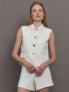Model wears a white collared tank with chunky gold buttons and symmetrical pockets below the waist.