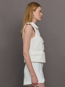 Model wears a white collared tank with chunky gold buttons and symmetrical pockets below the waist.