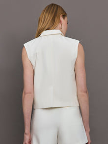 Model wears a white collared tank with chunky gold buttons and symmetrical pockets below the waist.