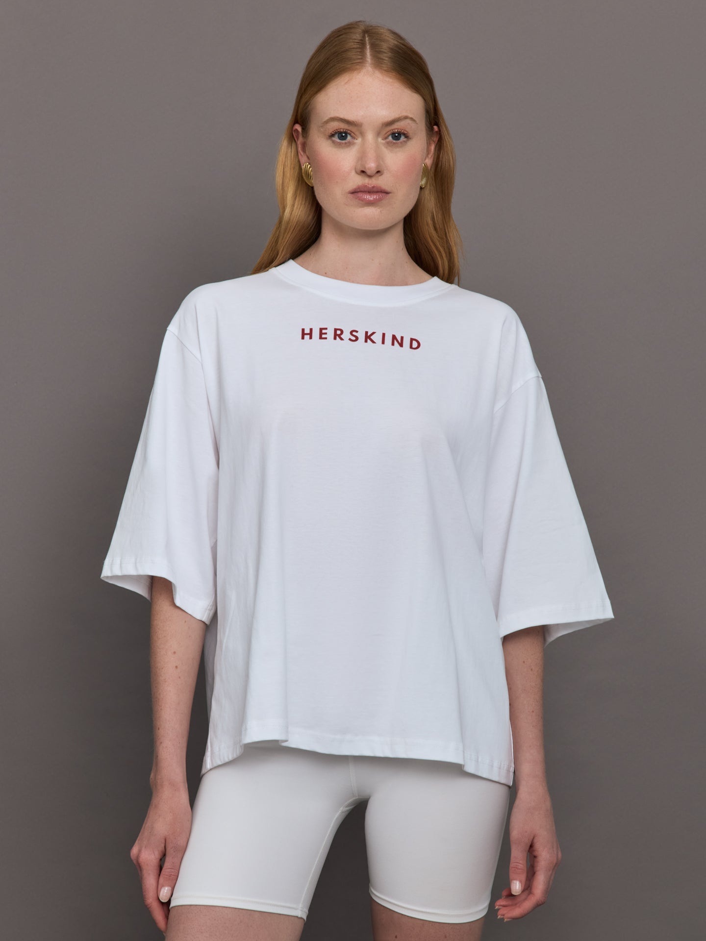 Model wears an oversized wide sleeve white tee shirt with red Herskind lettering across the chest.