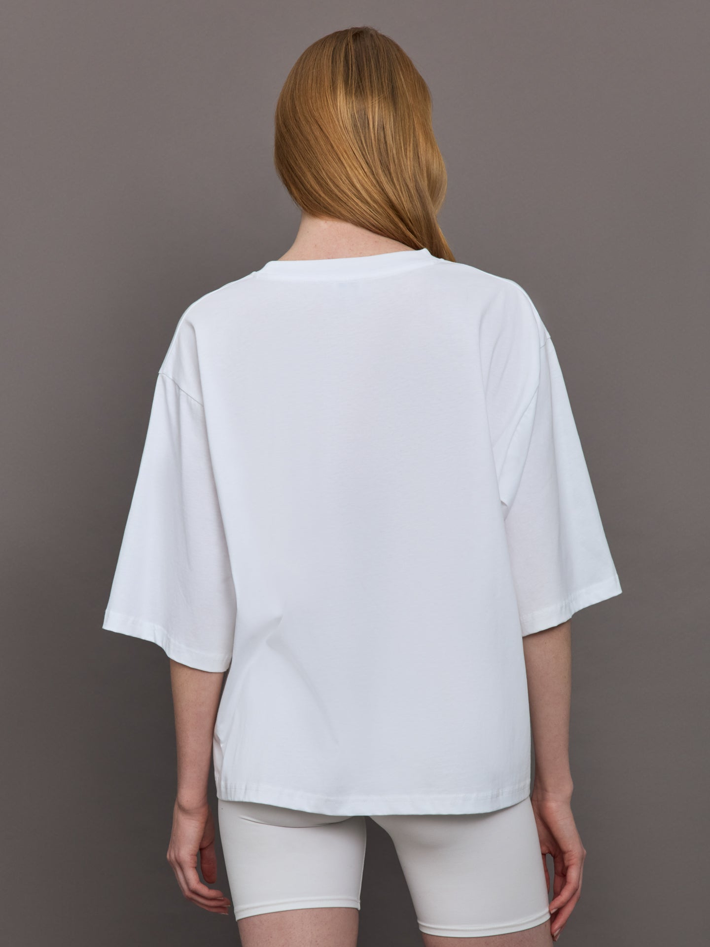 Model wears an oversized wide sleeve white tee shirt with red Herskind lettering across the chest.