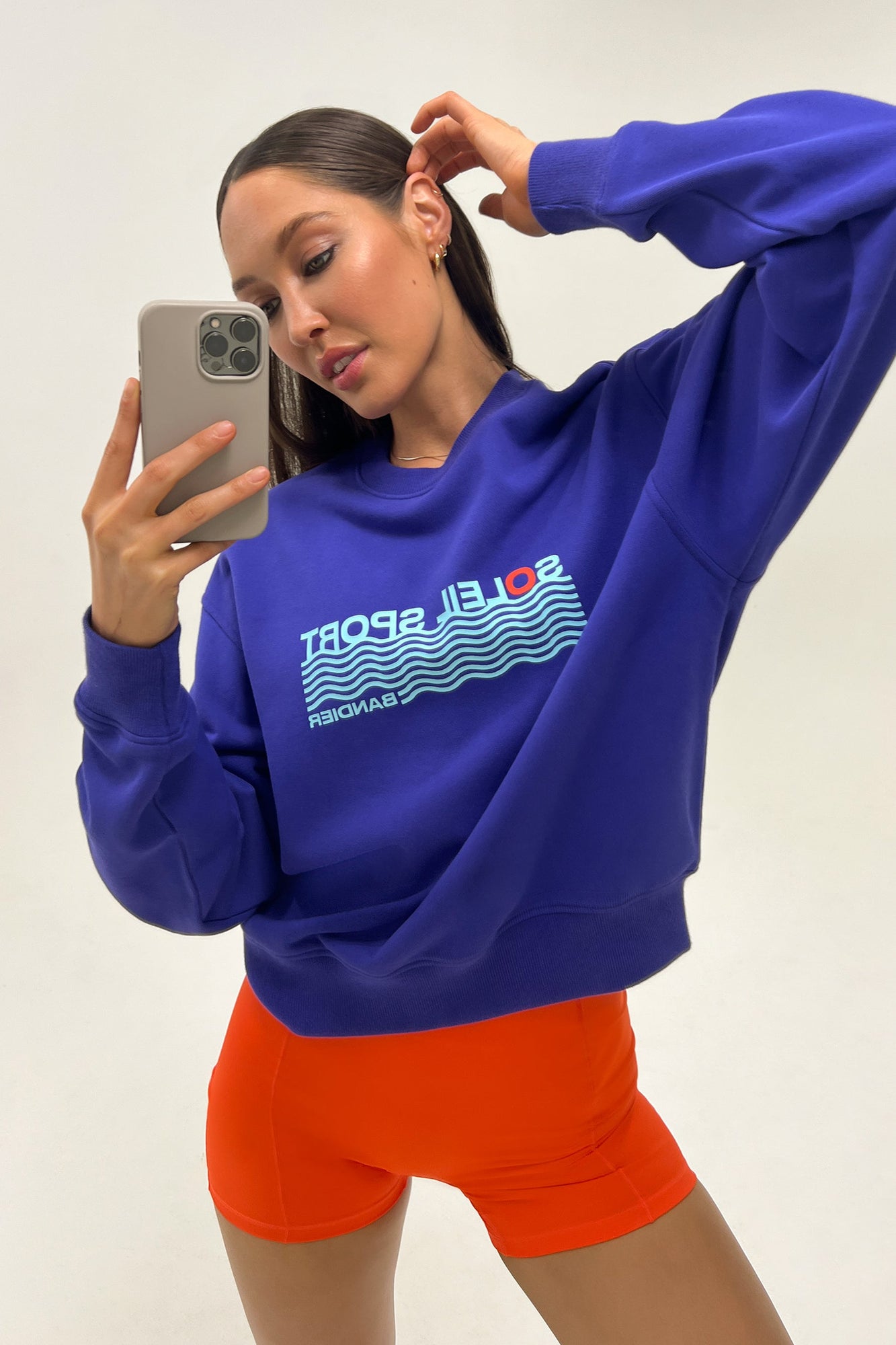 Model wears a royal blue crewneck sweatshirt with the lettering "Soleil Sport" across the chest with wavey lines below and "Bandier" in the bottom right corner. 