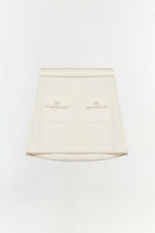 Cream mini skirt with lace trim, two front pockets with circular metal details, and curved hem.
