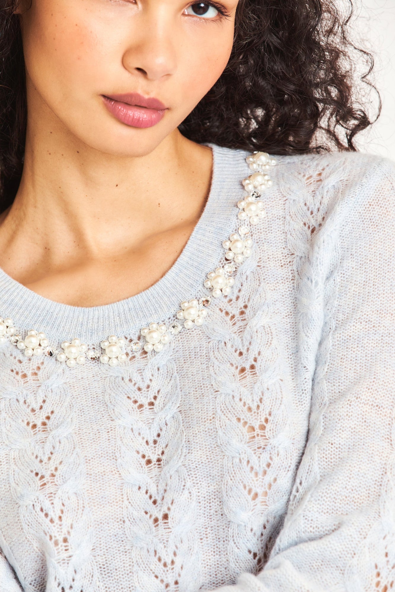 The lightweight baby blue cable knit sweater is a cashmere wool blended sheer fabric with pointelle detailing and a hand embellished neckline with crystals and clusters of iridescent pearls. 