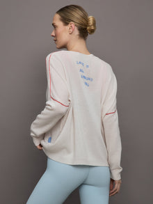 Model wears a white sweater with red seams along the biceps and blue block lettering on front bottom right that says LOVE. Back of sweater says in blue lettering 