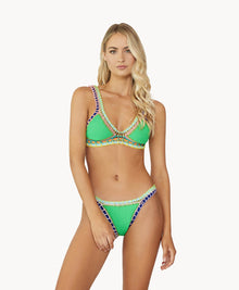 A blonde woman wearing a green bikini stands against a white wall. 