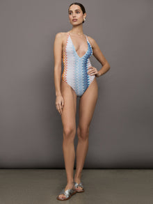 Model wears a one piece high cut bathing suit with a deep v neck and multicolored zig zag pattern. 