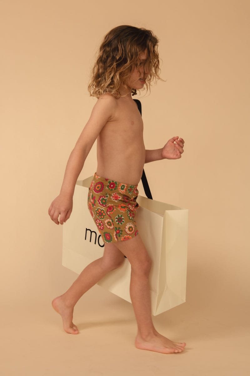 Child's swim trunk with multicolored floral print in red, yellow, and green on tan background.