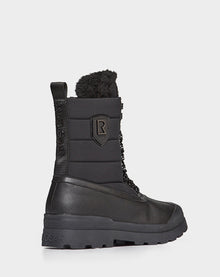 The REAGAN - 6222500 BLACK by Rudsak is a men’s black winter boot with a thick rubber sole, lace-up front, padded upper, faux fur collar, and Rudsak branding on the side and heel—crafted for comfort like premium leather boots.