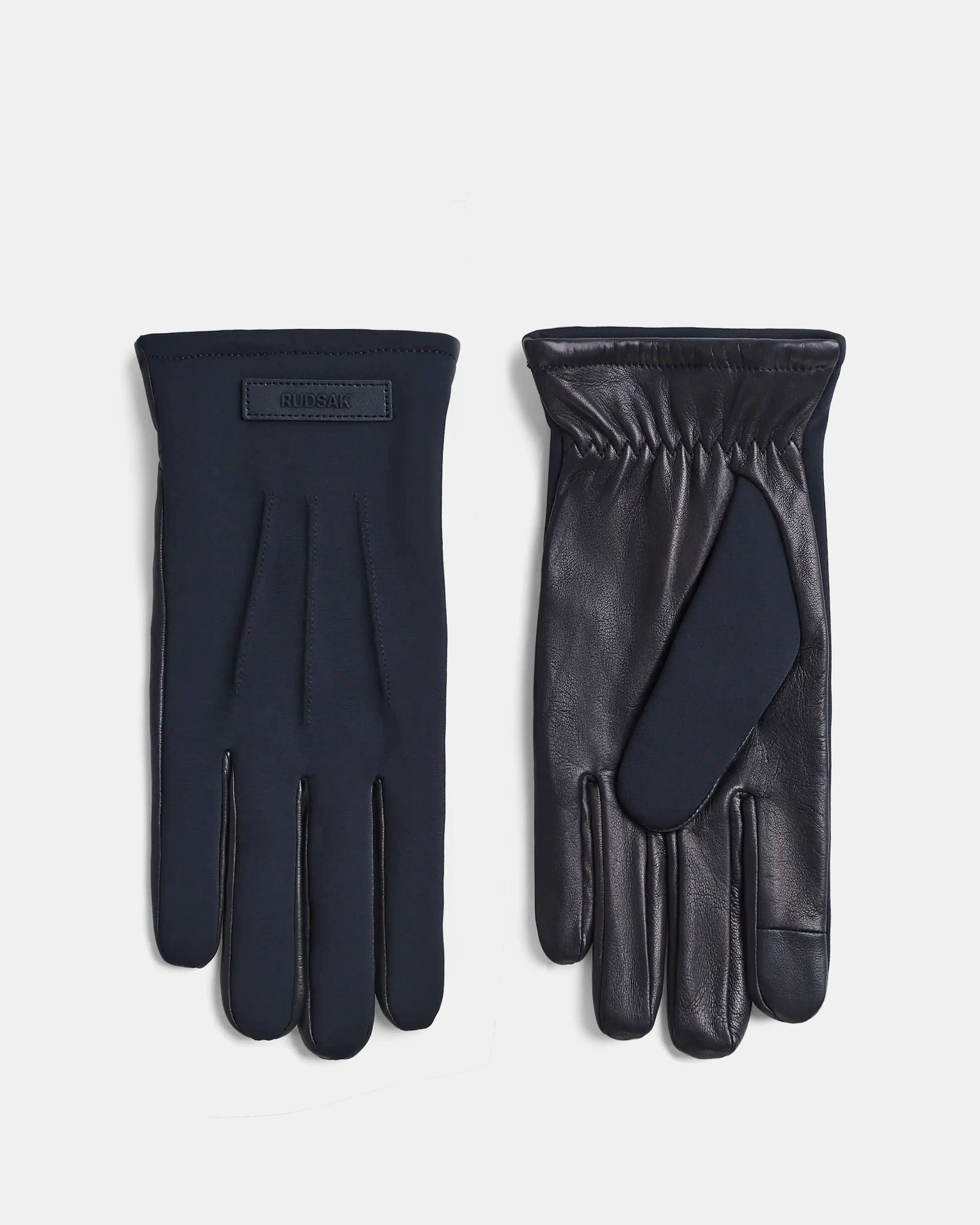 A pair of KRISTOPHER - 6423502 Black gloves by Rudsak is shown; one glove displays the front with a small tag, while the other reveals the palm sides smooth, shiny leather texture.