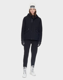 A person wearing Rudsak’s DEST - CA EN 6119516 BLACK down jacket stands facing forward in black gloves, black pants, a white beanie, and white lace-up boots against a plain light gray background.