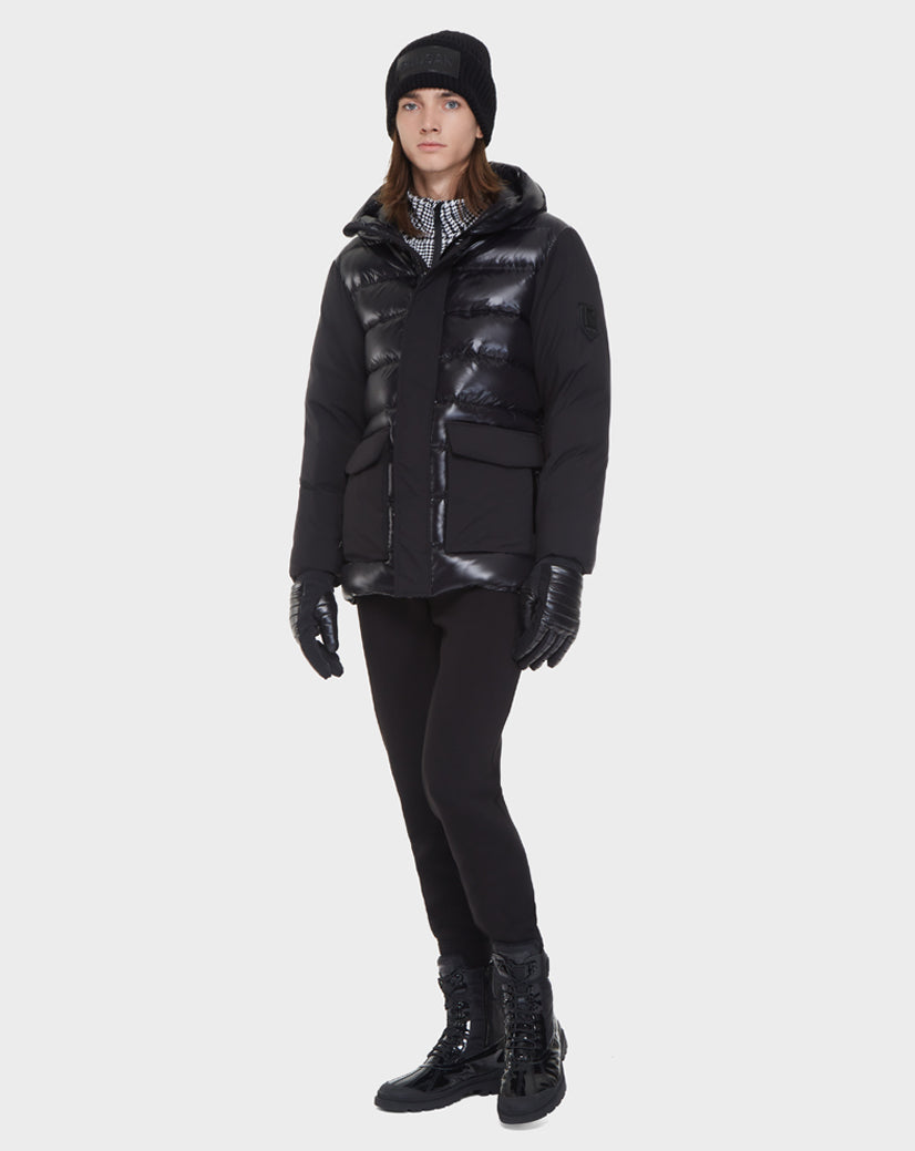A person stands against a plain white background wearing Rudsak’s DUSK - M121506 BLACK men’s puffer jacket with waterproof zippers, paired with a black beanie, gloves, pants, and boots.