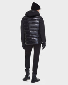 A person faces away, wearing the Rudsak DUSK - M121506 BLACK men's shiny black puffer jacket with waterproof zippers, along with a black beanie, gloves, pants, and shoes against a plain white background.