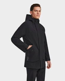 A man wears the Rudsak IAN - 6124009 Black rainwear jacket, featuring a high collar, zippered pockets, and a hood, with his right hand in the front pocket against a plain white background—blending function and style for rainy days.