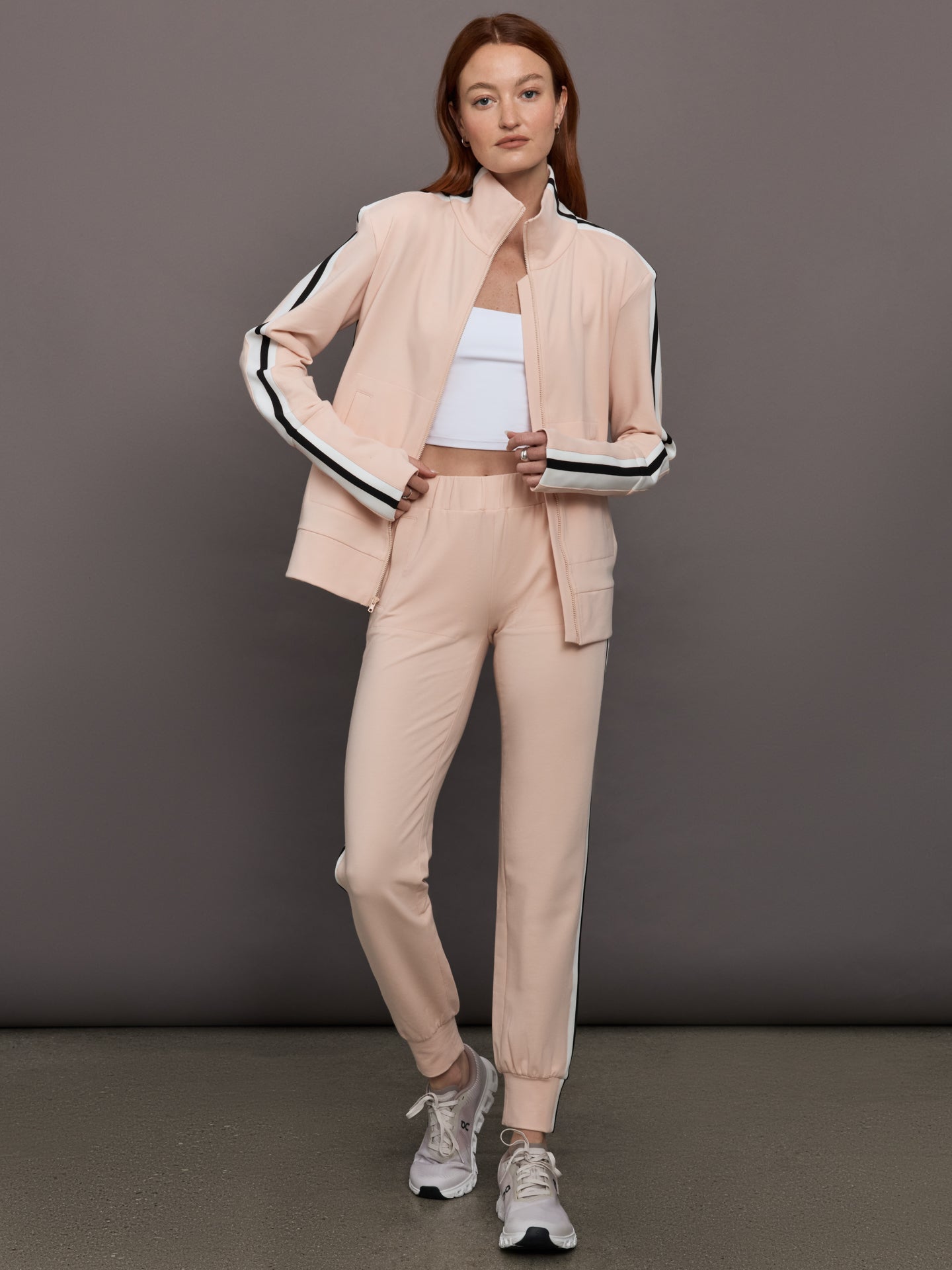Model wears baby pink jacket with a turtleneck, front zipper, and side stripes on the sleeves.
