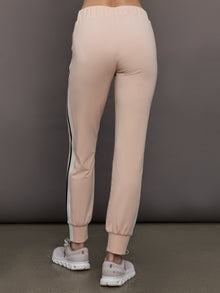 Model wears baby pink jogger pants with side stripes, elastic waistband, and cuffed ankles.
