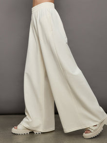 Model wears a pair of oversized wide leg cream colored sweatpants. 
