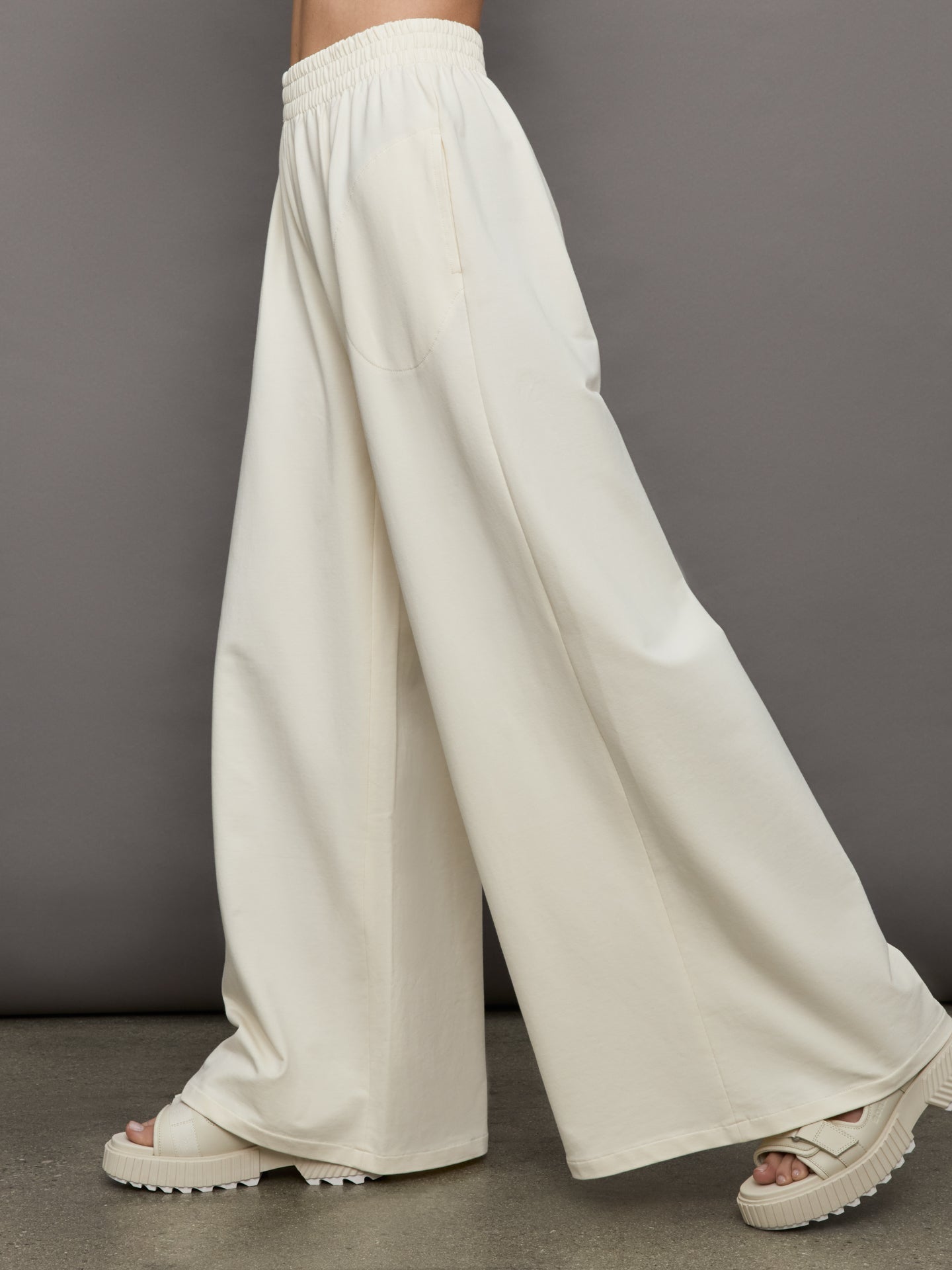 Model wears a pair of oversized wide leg cream colored sweatpants. 