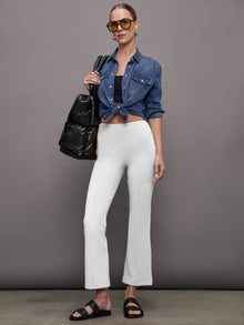Model styled in white flare pants with denim shirt and black sandals, full look.