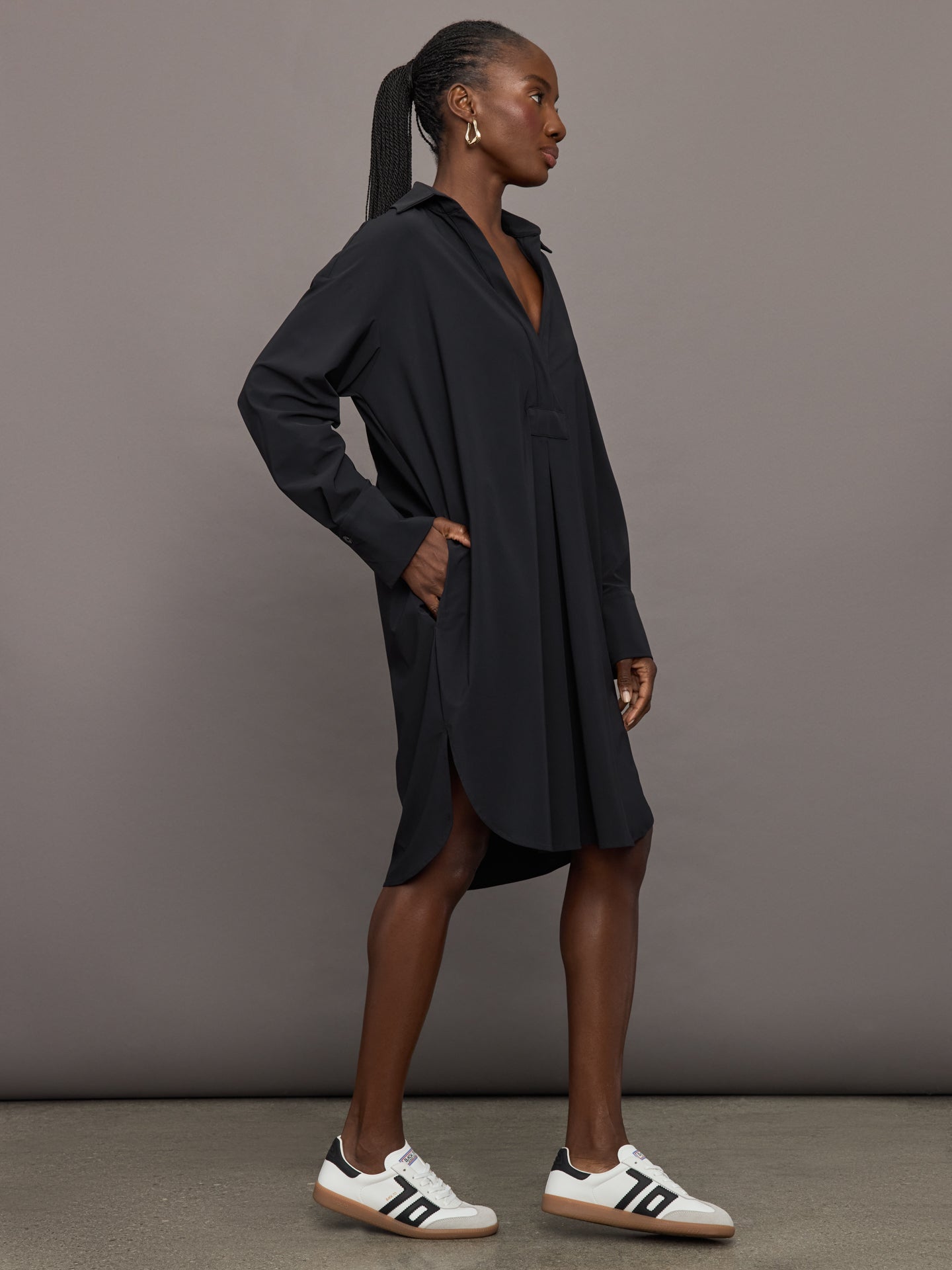 Side view of black shirtdress with oversized drape and long sleeves.