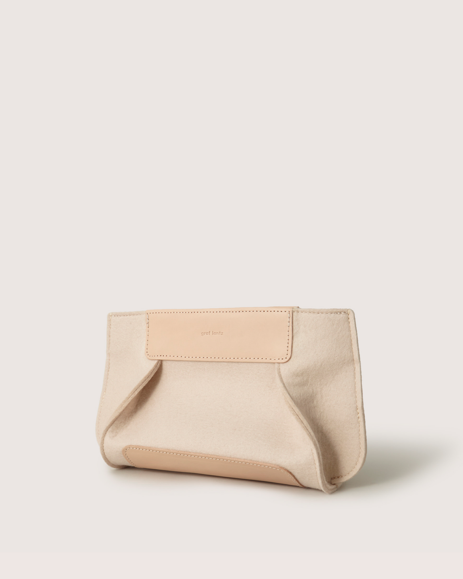 The Graf Lantz Frankie Merino Wool Clutch, showcasing a minimalist design and elegant beige and tan hues with a leather accent, stands out against a plain, light background, epitomizing sustainable fashion.