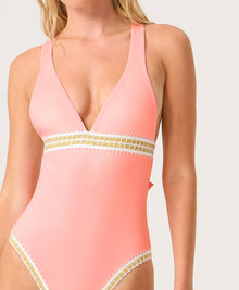 Woman wearing a pink one-piece swimsuit with gold trim on a white background