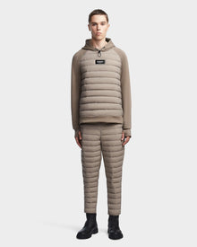 A person faces forward wearing the Rudsak MIKE - 6523503 Cement taupe puffer hoodie and insulated pants set with black lace-up boots, against a plain light background.