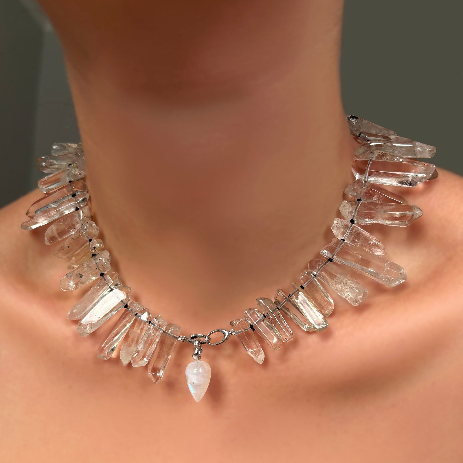 Rock crystal collar with white gold linking ovals clasp holding a rainbow moonstone drop charm on ripple bale on a model's neck.